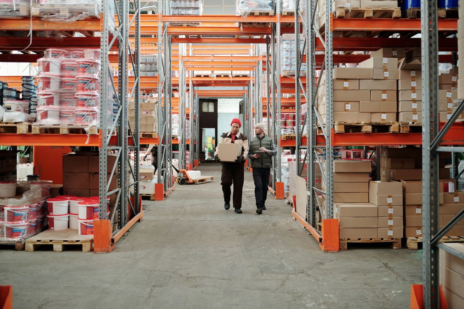 Two warehouse workers walking a racking aisle stacked with palletised goods