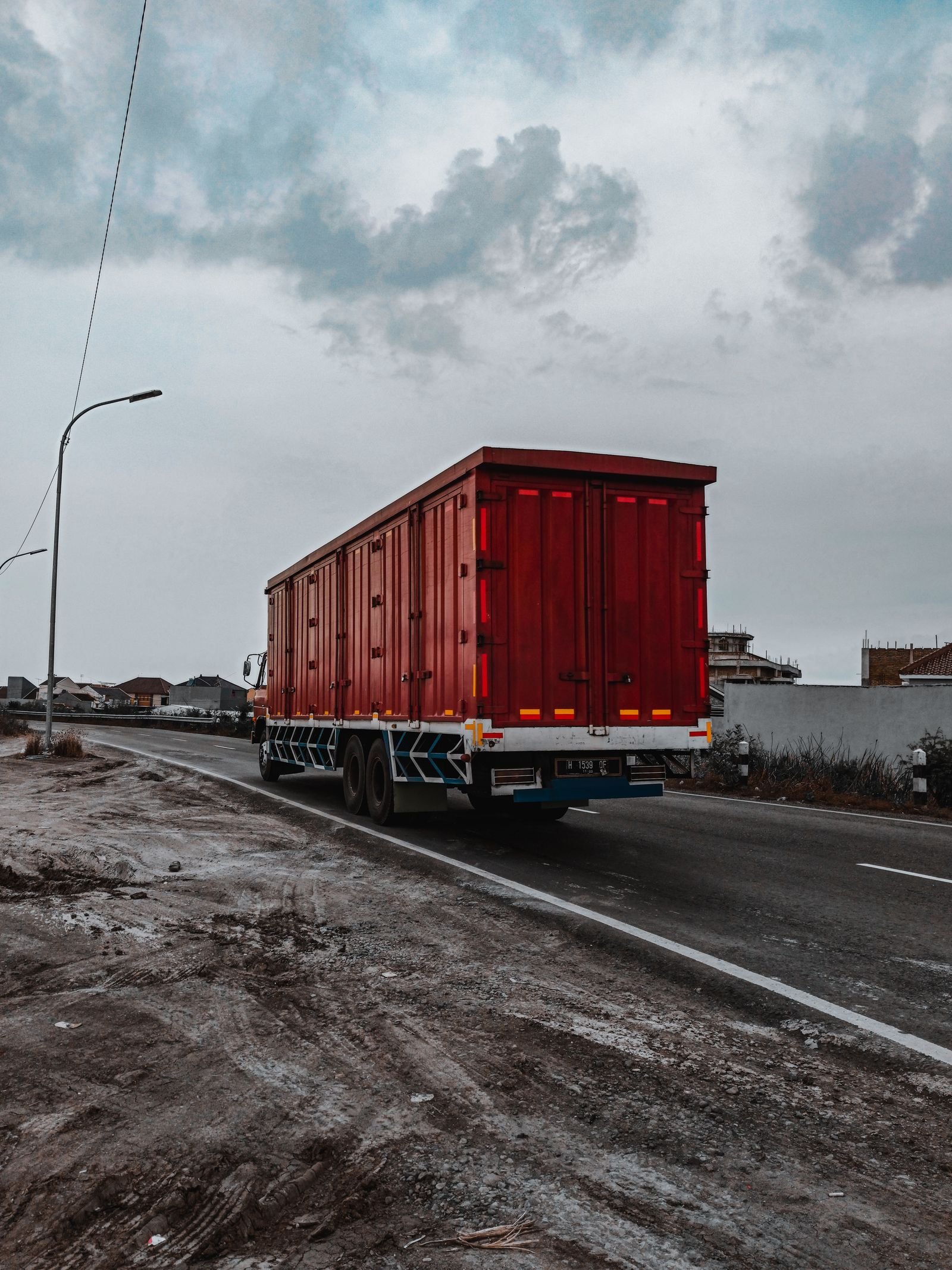 A red container truck on the road under an overcast sky