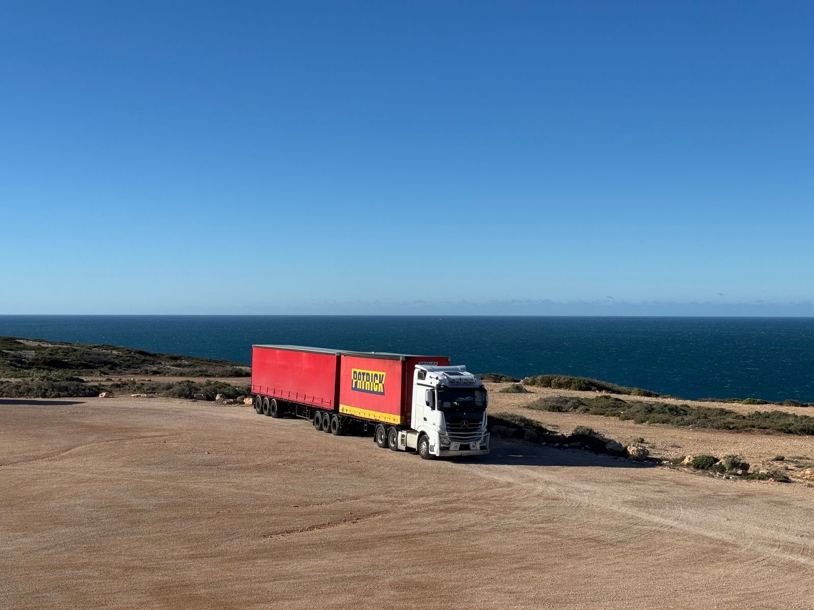A curtain-side trailer parked on a coastal road above the sea